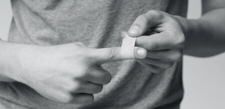 Man using adhesive tape on injured finger, self-treatment after trauma, close up, monochrome photo