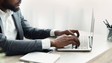 Unrecognizable african businessman working on laptop in modern office, hands typing on computer...