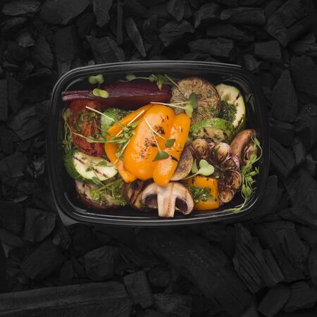 Grill cooked concept. Prepared vegetables in black plastic box for delivery on coal backgroundの写真素材