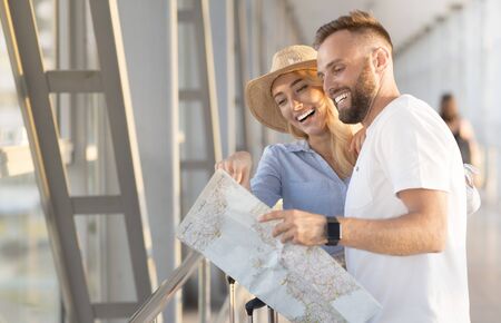 Happy couple observing map and discussing their vacation, waiting for departure, copy space