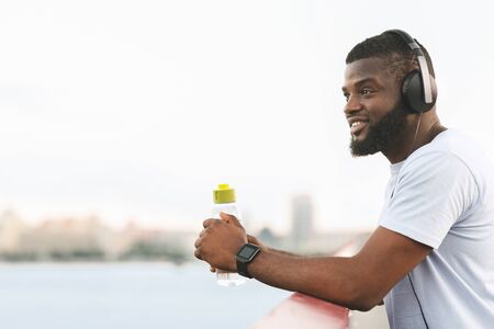 Smiling Black Man Having Rest On The Bridge, holding bottle of water, empty space