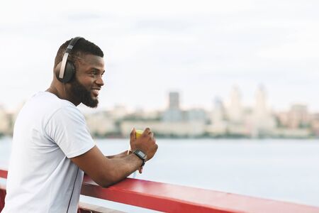 Handsome African American Sportsman Enjoying The City View From The Bridge, holding bottle of water,...