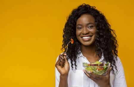Healthy Nutrition. Happy African American Lady Eating Vegetable Salad, yellow studioの写真素材