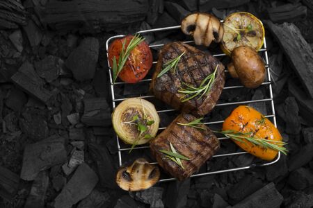 Flat lay of well done meat steak with vegetables on coals, copy space for text, black