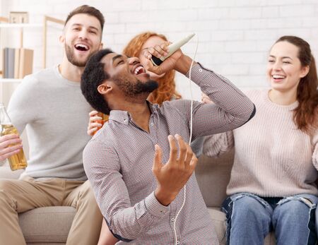 Young man holding microphone and singing at karaoke, having home party with friendsの写真素材