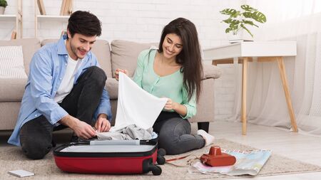 Loving couple packing clothes into suitcase, sitting on floor at homeの写真素材