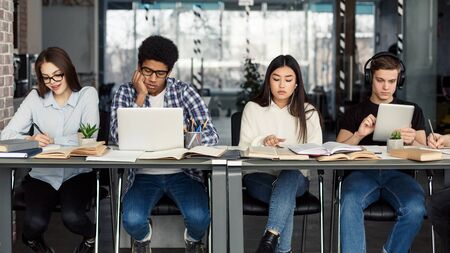 Students using different gadgets studying in university library and preparing for examsの写真素材