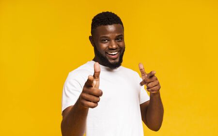 Flirty black man pointing at camera with both hands, yellow studio background