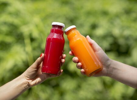 Summer chill. Two hands holding detox cocktails on green tree background outdoorの写真素材