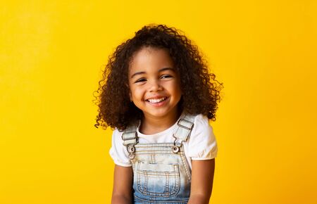 Happy african-american child girl smiling to camera over yellow backgroundの写真素材
