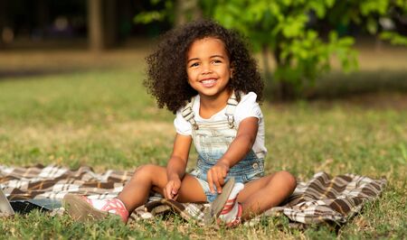 Adorable girl sitting on blanket at nature, enjoying summertime in the park, free spaceの写真素材