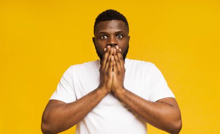 It cant be real. Shocked black guy shut his mouth in amazement, yellow backgroundの写真素材