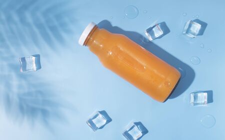 Summer drink. Refreshing summer detox cocktail in glass bottle with ice cubes and tropical leaf on blue backgroundの写真素材