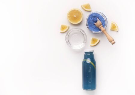 Creative blue detox water with fresh lemons, ice and natural dye flying above bottle on white background with copy spaceの写真素材
