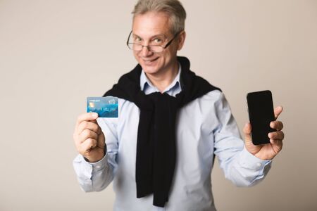 Senior man showing blank screen phone and credit card over grey backgroundの写真素材