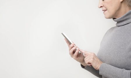 Active senior woman browsing on modern smartphone, isolated on light background, panorama with empty...
