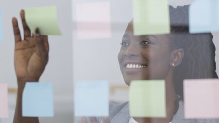 Business Ideas. Afro Businesswoman Putting Sticky Notes On Glass Visualization Board In Office....