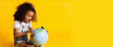 Early education. Little girl pointing to world globe, yellow background, copy spaceの写真素材