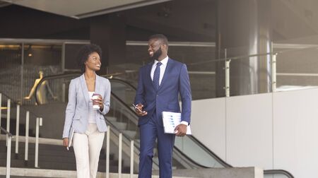 Two cheerful african american employees leaving office building for coffee break, panorama with copy...