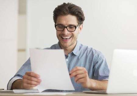 Man Reading Financial Report At Laptop Satisfied With Statistical Results Indoorの写真素材