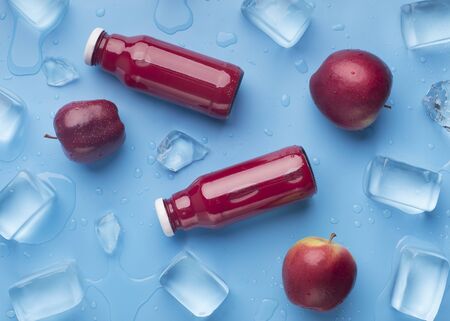 Summer healthy red drink in glass bottles with fresh apples on blue background with ice cubes