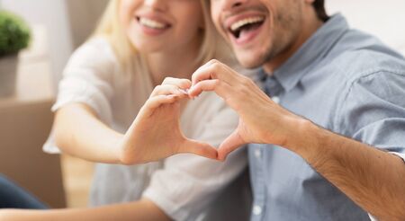 Unrecognizable Couple Gesturing Heart Shape With Hands Sitting And Hugging In New Apartment. Cropped, Panoramaの写真素材
