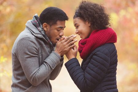 Man with breath warming woman hands, walking in autumn park