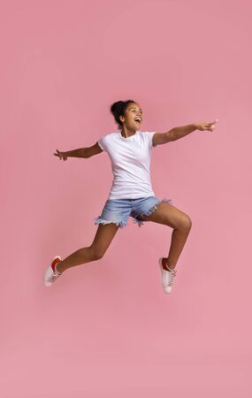 Portrait of african girl jumping and pointing finger aside on pink studio background, free spaceの写真素材
