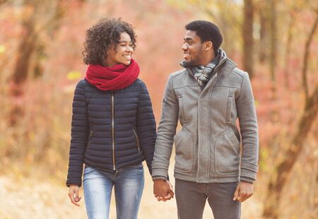 Loving afro couple walking in autumn park, looking at each otherの写真素材