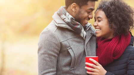 Happy african-american couple with cup in autumn park, having family picnic , free space