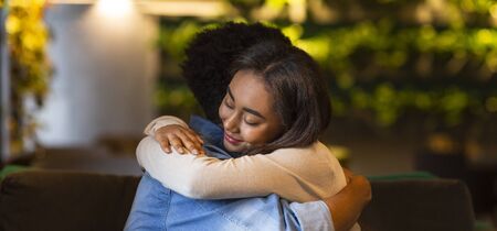 Warm hugs. Young mixed race girl hugging her boyfriend, cafe interior, copy spaceの写真素材