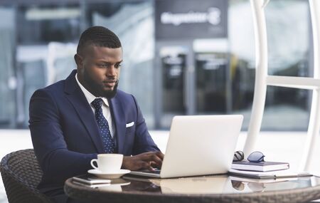 Serious African American Businessman Working On Laptop Computer In Outdoor Cafe In City Center. Free Spaceの写真素材