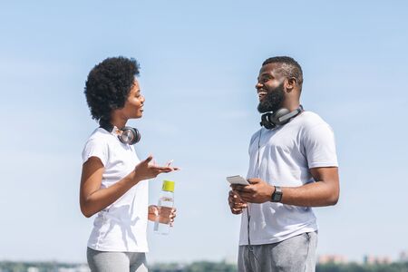 Jogging Coaching Concept. Happy Black Couple Talking About Morning Running Training Plan Near River Bank In City.の写真素材