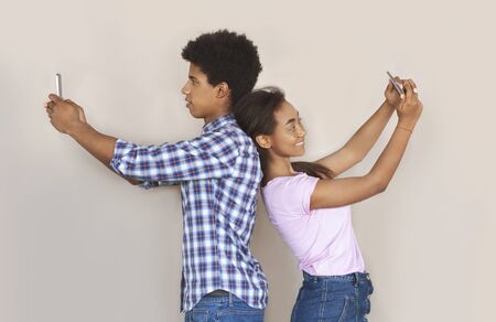 Gadget and social media addiction. Two african teenagers standing back to back, making selfie and ignoring each otherの写真素材