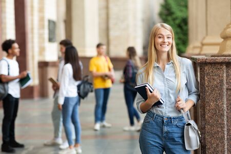 Happy girl posing to camera with books in college campus, having break between classesの写真素材