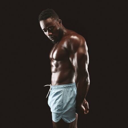 Side triceps pose perfomed by handsome african american bodybuilder, black studio backgroundの写真素材
