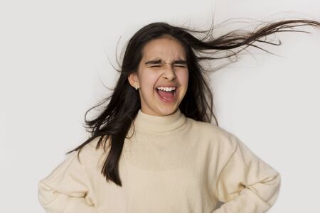 Joyful school girl shouting with flying hair over light backgroundの写真素材