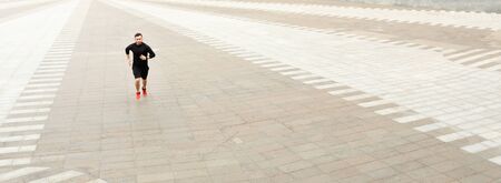 Young male athlete running in city center, training before marathon, panorama with copy spaceの写真素材