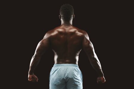 Unrecognizable african bodybuilder showing strong hands and back muscles, athletic trapezius, studio...