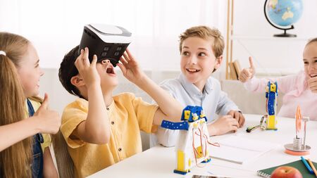 Schoolboy playing with vr glasses in classroom, having break at school