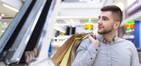 Consumerism concept. Guy with purchases walking in shopping center, copy spaceの写真素材