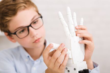 Smart schoolboy experimenting with humanoid robotic hand, developing his skills at stem lessonの写真素材