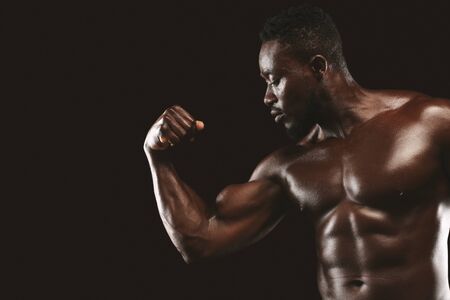 Handsome african american male bodybuilder demonstrating his arm musculs over black background, free spaceの写真素材