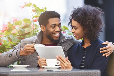 Cheerful black couple shopping online at cafe, using tablet, drinking coffee, copy spaceの写真素材