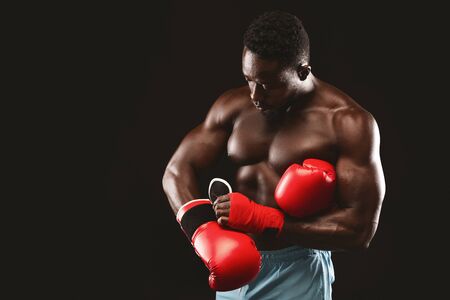 African american muscular boxer getting ready for fight, wearing red gloves, black background, free spaceの写真素材