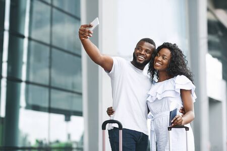 Vacation begins. Happy african couple taking selfie, waiting for flight near airport building, free...
