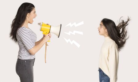 Furious mother shouting at girl through loudspeaker over light background, side viewの写真素材