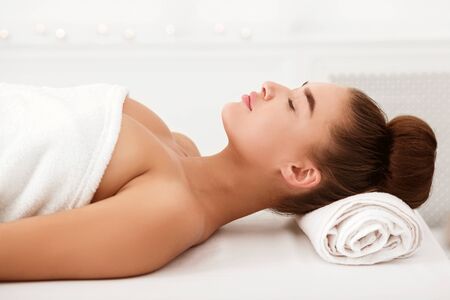 Beautiful young woman relaxing in light spa salon, waiting for cosmetology procedure, side viewの写真素材