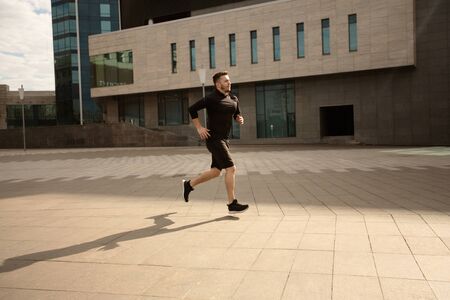 Sporty man running outdoors, having cardio training against urban cityscape, side viewの写真素材