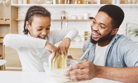 Excited african father and his joyful daughter playing with dough while making pastry at kitchen